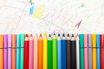 Multi-colored pencils lie on white paper drawn with multi-colored curved lines.