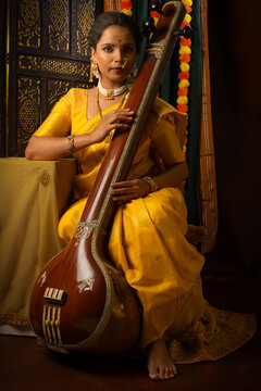Young India woman in yellow saree holding the musical instrument called as Tanpura or Tambora and sitting in the musical mood.