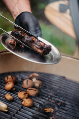 Grilling beef ribs and mushrooms on barbecue grill.