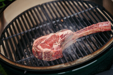 Grilling juicy Tomahawk steak on barbecue grill with smoke rising.
