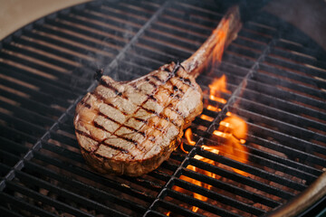 Grilling juicy Tomahawk steak on barbecue grill with smoke rising.