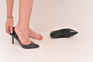 A slender young woman puts on black shoes. empty space