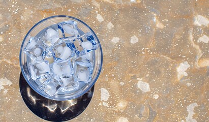 Melting ice cubes in a plastic cup placed on a reflective surface near a pool on a sunny day
