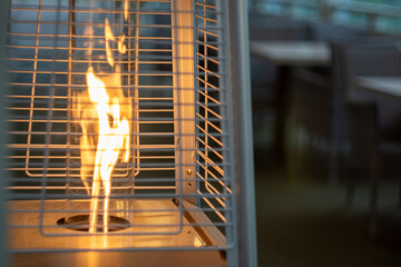 Outdoor patio heater with flame enclosed in protective mesh on a cozy evening