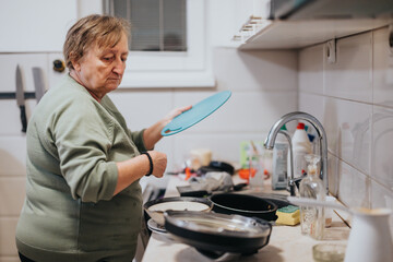 A senior woman organizing and tidying a kitchen, focusing on a task that demonstrates focus and care within a domestic environment.