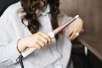 Young teenage woman curling her hair with a curling iron at home.