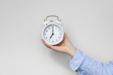 Woman hand holding white alarm clock on white background. Seven o'clock.