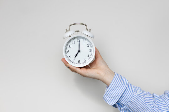 Woman hand holding white alarm clock on white background. Seven o'clock.