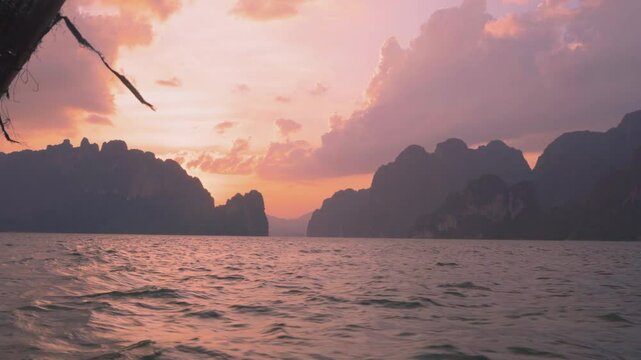 Boat trips to the islands of Cheo Lan Lake. Colorful orange sunset and mountain landscape on the background of running waves, taken from a boat. Travel and tourism in Thailand.