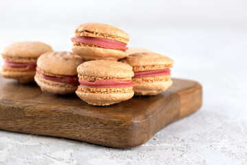 Vegan homemade caramel macarons with raspberry cream on shea butter on a wooden board on a light table. Sugar, lactose and gluten free.