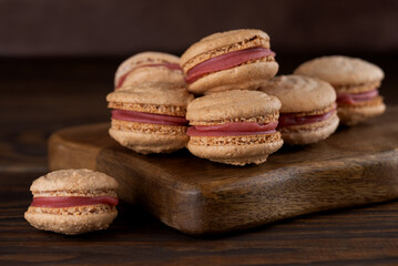 Homemade caramel macarons with raspberry cream on shea butter on a brown wooden board. Sugar, lactose and gluten free. Vegan dessert.