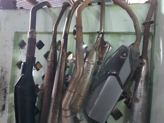 A collection of rusty and used motorcycle exhaust pipes leans against a wall.  The pipes show various states of wear and discoloration.