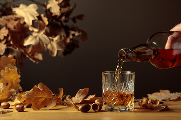 Whiskey with ice on a wooden table with dried-up oak leaves.
