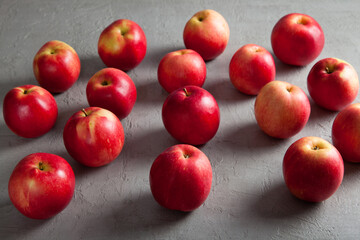 A group of fresh red apples is scattered across a gray textured surface, creating a clean and minimalistic top-down food composition ideal for seasonal and natural product themes.