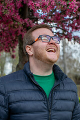 A joyful Caucasian man revels under cherry blossoms, celebrating Hanami's fleeting beauty and...