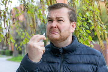A perplexed Caucasian man grimaces under verdant boughs, clutching pollen, embodying Allergy Awareness Week and peculiar springtime rituals
