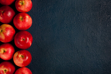 Multiple red apples arranged vertically on the left side over a dark blue textured surface. Perfect background image for food-themed content, healthy lifestyle promotions, and seasonal designs.