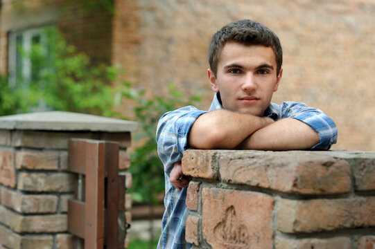 portrait of a thoughtful young man leaning against a brick fence