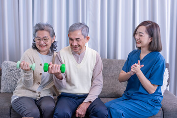 senior couple doing dumbbell exercise with nurse or physiotherapist in uniform in applause for...