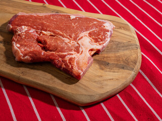 Fresh uncooked T bone steak on a wooden cutting board and on classic red and white stripe table...