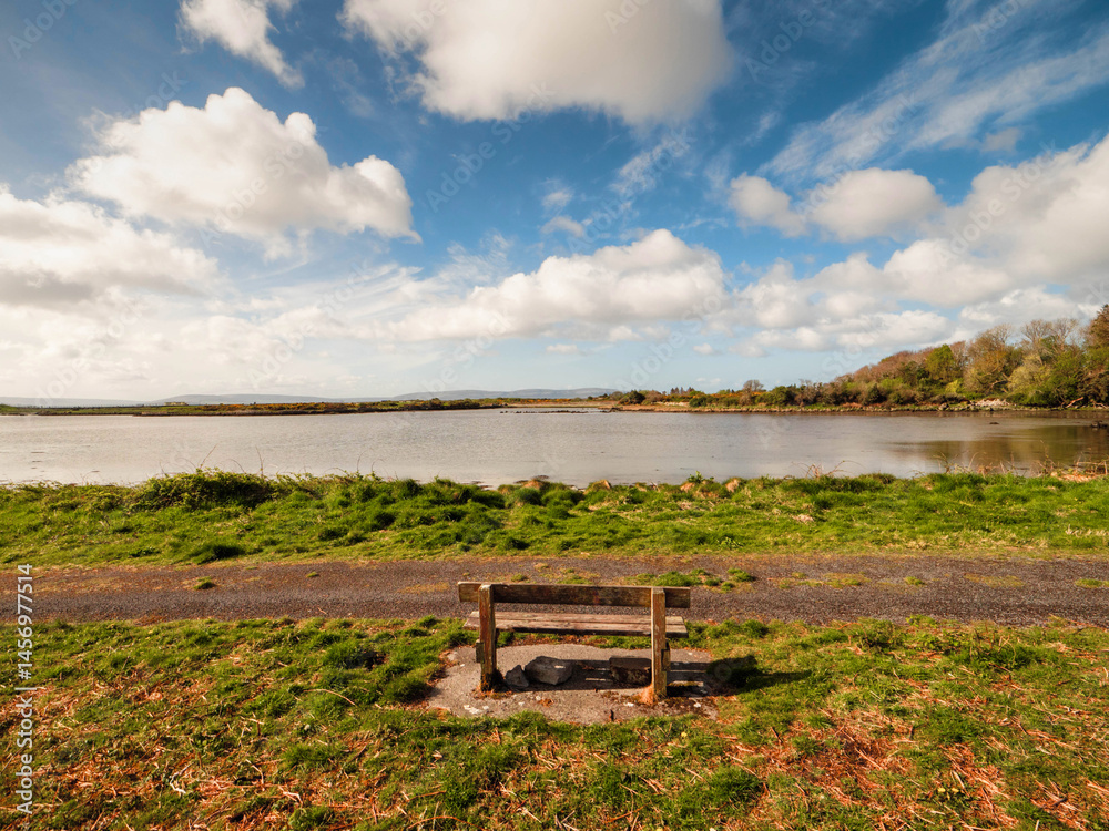 Fototapete one wooden old bench by a walking path with stunning view on open space with lake and amazing blue c
