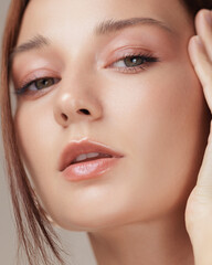Fototapeta premium Studio close-up of a woman with peach-toned makeup and radiant skin gently touching her face. Ideal for beauty, wellness, and high-end skincare or cosmetic advertising visuals.