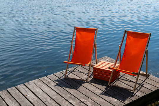 Two orange deck chairs sit on a wooden dock by a calm lake