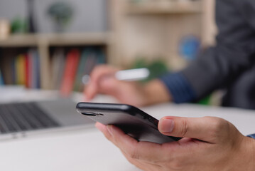 Hand holding smartphone with laptop in background. Concept of multitasking, online communication, and modern office technology.