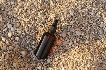 Close-up of a brown mockup of a glass jar of serum with a dropper on a small pebble on the beach. Concept of natural cosmetics for face care, wrinkle reduction, moisturizing. Image for your design
