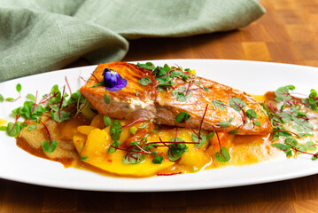 Seared salmon fillet with mango sauce. Gourmet seared salmon served on mango sauce, garnished with microgreens and edible flower, presented on a white plate.