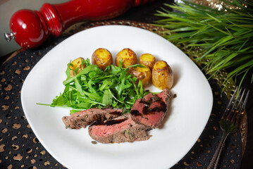 Medium rare steak with potatoes and arugula. Delicious plated meal featuring sliced medium rare steak, roasted baby potatoes, and fresh arugula salad with balsamic glaze.