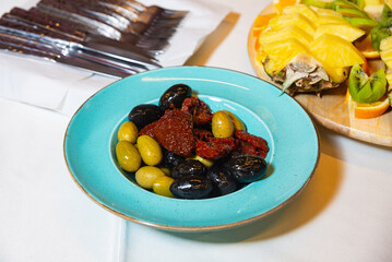 Mixed olives and sun-dried tomatoes appetizer. Colorful bowl with green and black olives and sun-dried tomatoes served as a Mediterranean appetizer on a turquoise plate.
