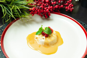 Panna cotta dessert with caramel and berries. Elegant panna cotta topped with caramel sauce, fresh raspberries, and mint leaves served on a white plate with red trim.