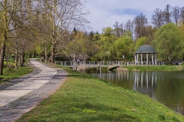 A beautiful city park with well-kept paths, a pond and a gazebo on the shore in spring.