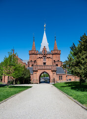 Entrance gate and stone walls of Hradec nad Moravici Castle in the Czech Republic, showcasing Gothic revival architecture surrounded by greenery in a peaceful historic setting.