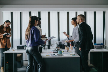 A team of business professionals engaged in a discussion around a table inside a modern office. This image depicts teamwork, collaboration, and productivity in a formal work environment, conveying