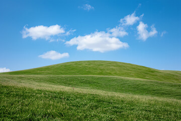 Obraz premium a green hill with a blue sky and clouds