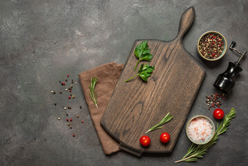 Culinary background with wooden cutting board, cherry tomatoes, spices and herbs on dark rustic background, top view, flat lay