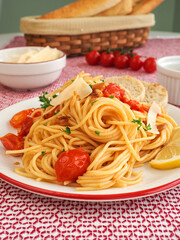 Plate of spaghettini with cherry tomato with bowl of shaved parmesan, basket of bread sticks, and fresh cherry tomatoes on-stem in the background