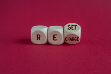 Wooden cubes form the expression Reset Recharge. Beautiful red background. Business reset and...