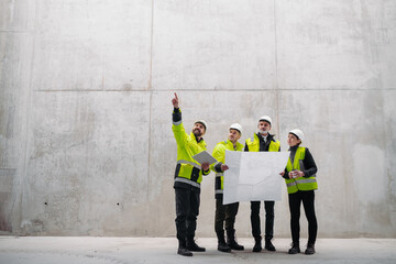 Team of engineers and construction workers reviewing blueprints, building site.