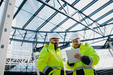 Construction managers using digital tablet on site, reviewing project plans.
