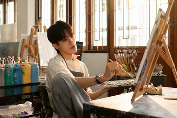 A young artist sits and draws, working on his new art project in his studio.