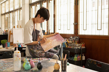 A young man in an apron sits at a table, drawing.