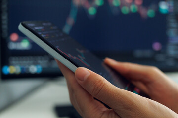 A person's hands cradle a smartphone displaying a stock market analysis chart with red and green indicators, set against a softly blurred backdrop.