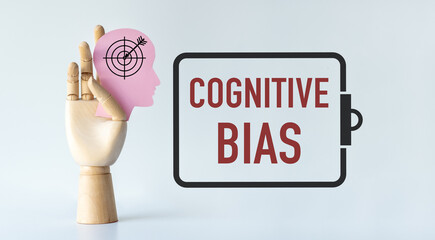 A hand holding a pink head with an arrow pointing to the right. The word Cognitive Bias is written below the image