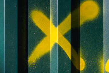 Vibrant yellow spray-painted cross against a textured green metal panel