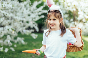 Easter egg hunt. Girl child Wearing Bunny Ears Running To Pick Up Egg In Garden. Easter tradition. Baby with basket full of colorful eggs.