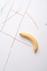 Single banana on white marble with gold veining – minimalist food composition for health, design, and editorial use