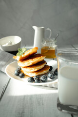 Cottage cheese pancakes with blueberries and sour cream on a white wooden table